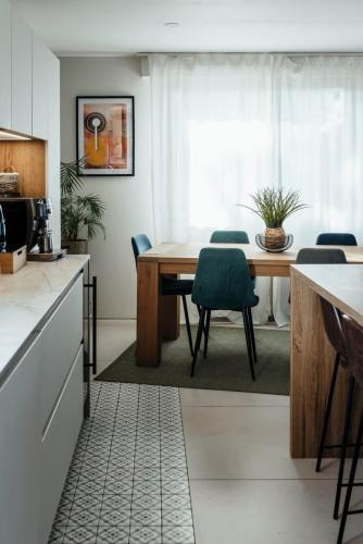 Espace repas dans une cuisine rénovée avec table en bois, chaises vertes, voilages blancs et carrelage à motifs.