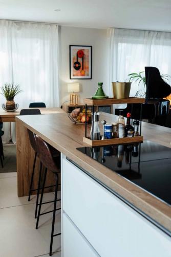 Espace repas dans une cuisine rénovée avec table en bois, chaises vertes, voilages blancs et carrelage à motifs.