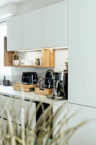 Cuisine contemporaine avec façades blanches, niches éclairées en bois, crédence végétale et plan de travail effet marbre.