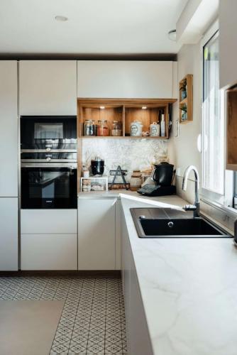 Vue de face d'une cuisine contemporaine avec îlot central en bois, façades blanches et électroménager noir intégré.