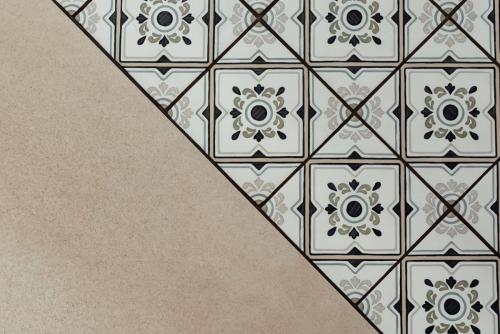 Détail du raccord entre un carrelage beige grand format et des carreaux de sol à motifs géométriques noirs et gris.