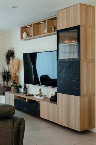 Meuble TV sur mesure associant bois clair, façades effet marbre noir, niches décoratives et porte vitrée striée.