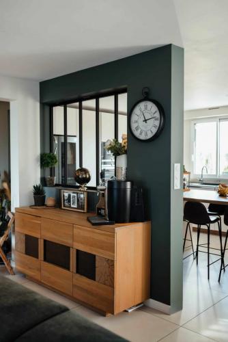 Mur vert profond avec verrière noire séparant visuellement le séjour de la cuisine, accompagné d'un buffet en bois clair.