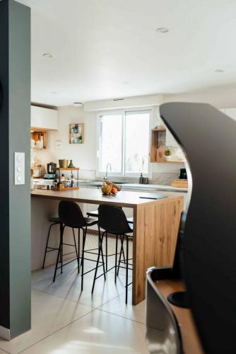 Cuisine rénovée blanche et bois avec grand îlot central, espace repas et tabourets hauts noirs.