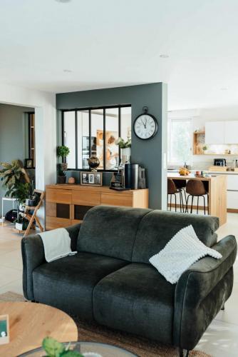 Salon rénové à Houppeville avec canapé vert, buffet en bois, verrière noire et nouvel accès à la cuisine.